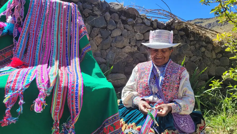 Una mujer realiza obras de artesania, ataviada con el traje típico