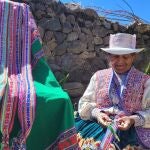 Una mujer realiza obras de artesania, ataviada con el traje típico