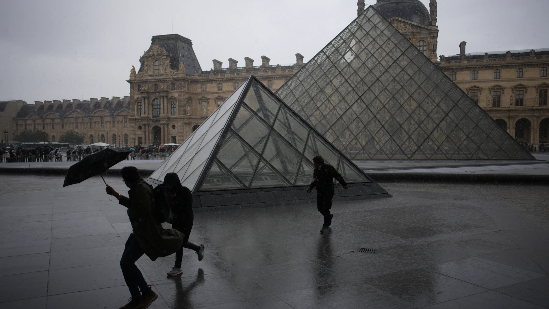 People run away in the rain in the courtyard of Le Louvre museum during rainfall Monday, Oct. 27, 2025 in Paris. (AP Photo/Christophe Ena)