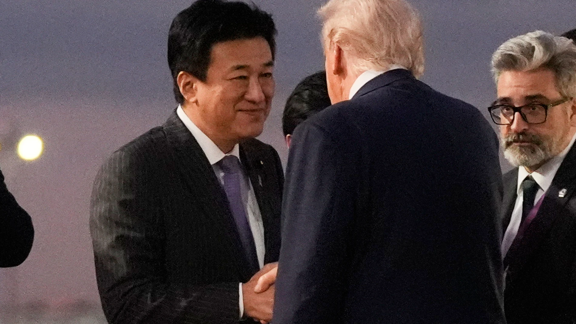 El secretario jefe del Gabinete de Japón, Minoru Kihara (izquierda), estrecha la mano del presidente Donald Trump al descender del Air Force One en el aeropuerto de Haneda, Tokio, Japón