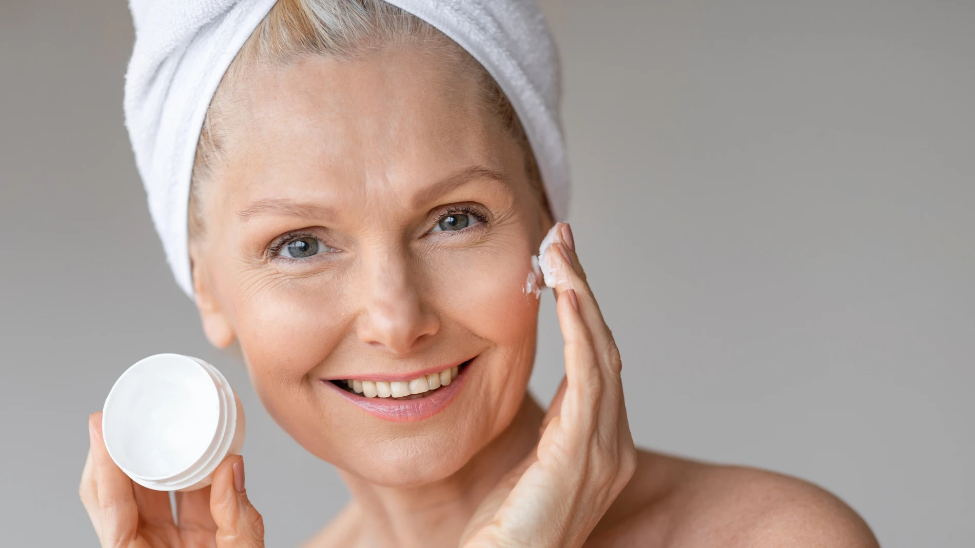 Mujer aplicando crema hidratante en el rostro durante su rutina de cuidado facial para piel madura.