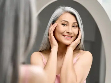 Tatcha, la firma japonesa que ha hecho del cuidado de la piel madura todo un ritual Mujer de cabello canoso frente al espejo, con piel luminosa y expresión relajada.