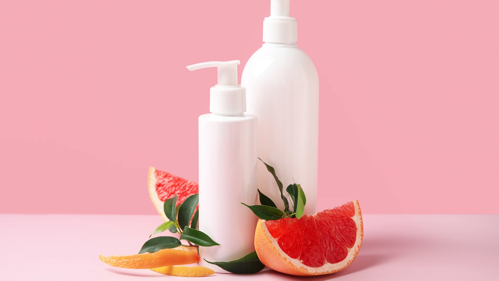 Cosméticos con fondo rosa y rodajas de pomelo