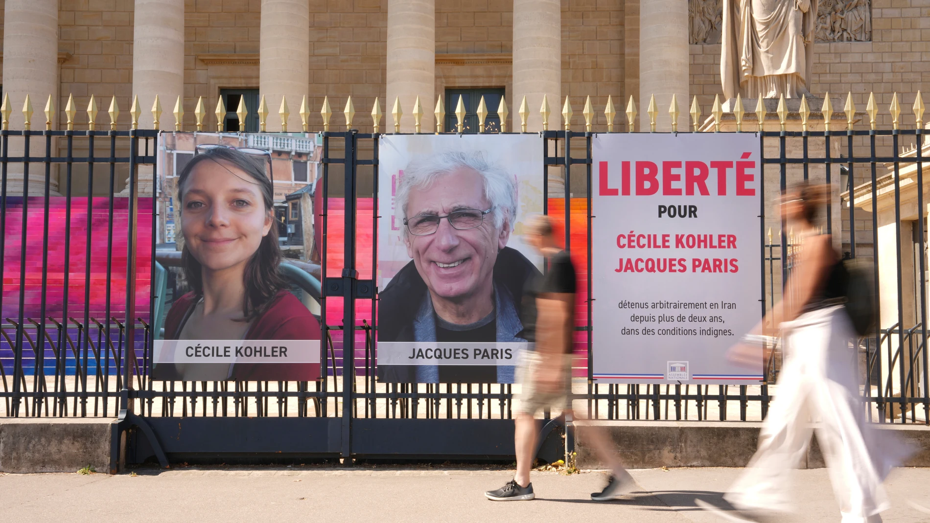 Personas pasan junto a los retratos de los ciudadanos franceses Cecile Kohler y Jacques Paris frente a la Asamblea Nacional francesa en París