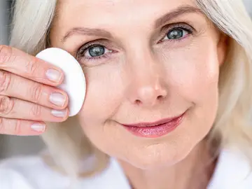 No son cremas, son desmaquillantes: el truco real para evitar las arrugas en el contorno de ojos Mujer madura desmaquillándose el contorno de ojos con un disco de algodón.