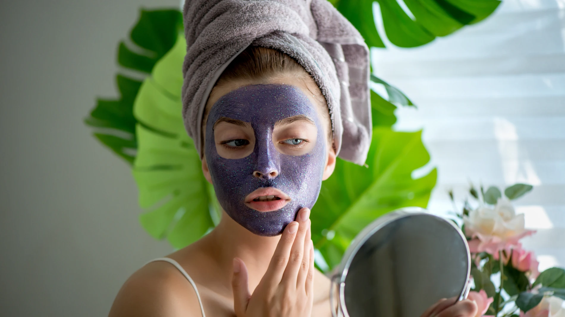 Mujer con mascarilla facial violeta frente al espejo, durante su rutina de cuidado facial.