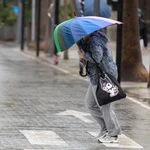 Una persona se resguarda con un paraguas de la lluvia y el viento