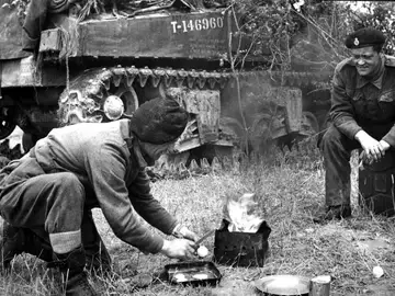 Unos soldados preparan comida y bebida junto a un tanque Unos soldados preparan comida y bebida junto a un tanque