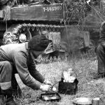 Unos soldados preparan comida y bebida junto a un tanque