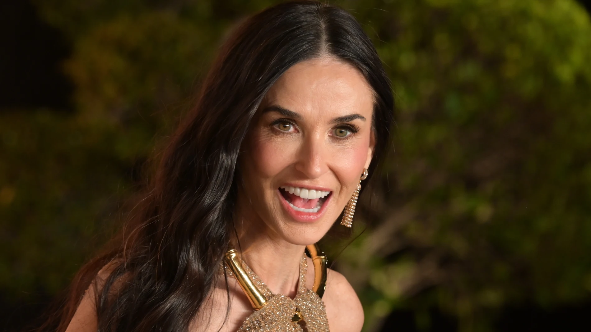 Demi Moore en un evento reciente, sonriendo con gesto natural y luciendo un vestido dorado
