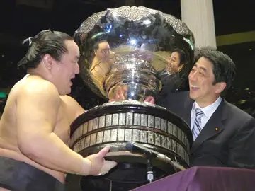Japan Sumo Takaichi Explainer FILE - Grand champion Asashoryu of Mongolia, left, receives the Prime Minister's Cup from Chief Cabinet Secretary and soon-to-be Premier Shinzo Abe at Tokyo's Ryogoku Sumo Arena on Sept. 24, 2006. (Kyodo News via AP, File)