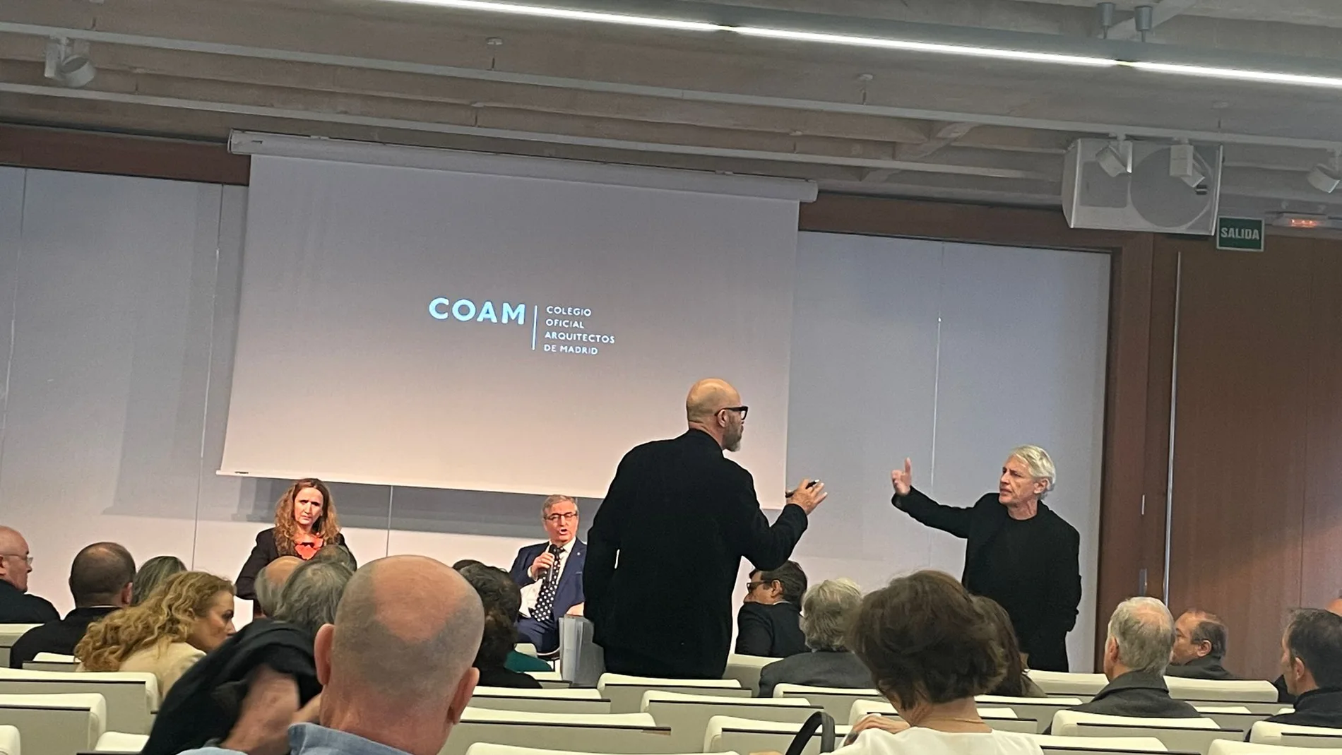 El decano del COAM, sigfrido Herráez (sentado), y otro miembro del Colegio, se enfrentan a Jesús San Vicente (en el centro), durante el acto de toma de posesión