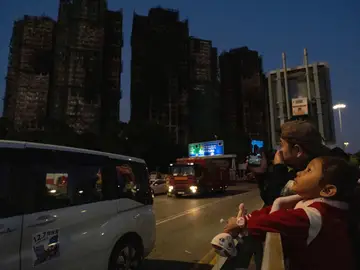 Hong Kong Fire A child holding a doll looks out at charred buildings burnt after a deadly fire that started Wednesday at Wang Fuk Court, a residential estate in the Tai Po district of Hong Kong's New Territories, Friday, Nov. 28, 2025. (AP Photo/Ng Han Guan)