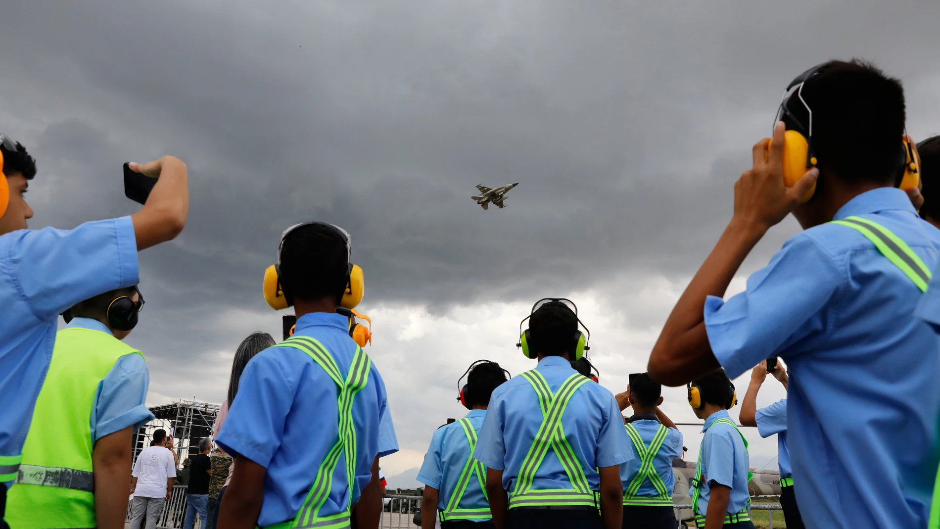 Estudiantes de mecánica aeronáutica observan un vuelo de exhibición de aeronaves militares durante una exposición de aviación en la Base Aérea Libertador en Maracay, Venezuela