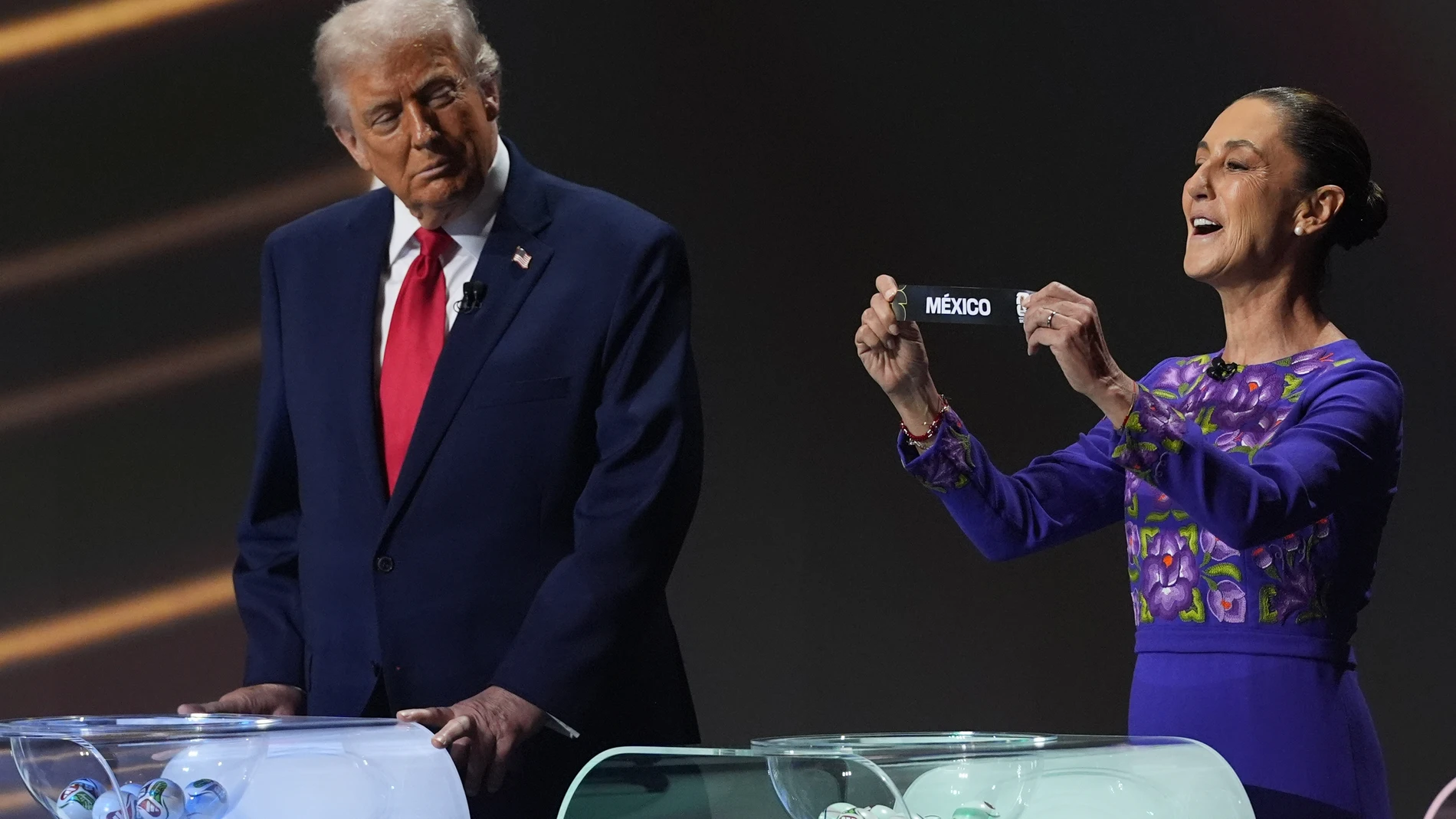 President Donald Trump looks across as Mexican President Claudia Sheinbaum holds up the team name of Mexico during the draw for the 2026 soccer World Cup at the Kennedy Center in Washington, Friday, Dec. 5, 2025. (AP Photo/Jacquelyn Martin)