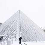 Un transe&uacute;nte caminando por los alrededores de un Museo del Louvre nevado
