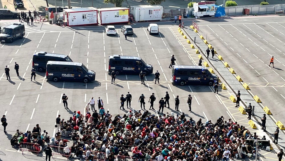 CEUTA, 20/08/2026.- Migrantes aguardan para poder acceder al centro provincial instalado en la zona de 'Loma Colmenar' en Ceuta tras habilitarse un espacio para su acogida este jueves. El Gobierno ha habilitado temporalmente varios espacios para la acogida de 1.800 personas migrantes que se encuentr